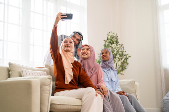 Muslim family wearing hijab video call greeting with relatives on smartphone smiling together at home, digital connection modern communication, arabic family with social platform, islamic content