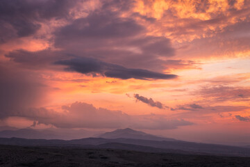 View of a vibrant sunset paints the sky with fiery oranges and soft purples, casting a warm glow over the distant mountain range, Kyrgyzstan.