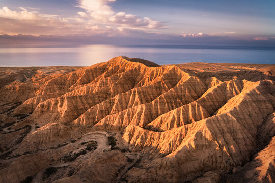 Aerial view of jagged, sun-kissed ridges cascade towards a tranquil sea under a pastel sky, a serene dance of earth and water, Bosteri, Issyk-Kul, Kyrgyzstan. - Powered by Adobe
