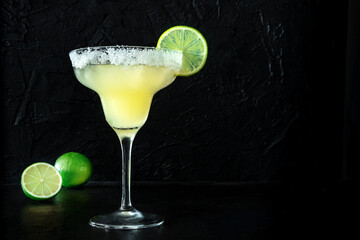 Margarita cocktail in the classic glass, side view on a black background, with limes and a salt rim, with a place for text