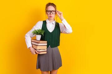 Student Holding Books and Plant in Front of Yellow Backdrop, Wearing Vest, Demonstrating Academic...