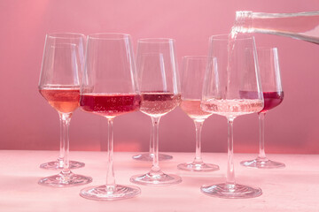 Rose wine poured from a bottle into a glass, wine tasting, a variety of hues and tints, side view on pink