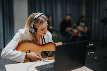 A guitarist wearing headphones plays an acoustic guitar in a professional studio. Other band...