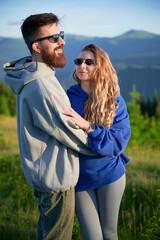Portrait of couple stand close together in scenic meadow with mountains in background. Man and...