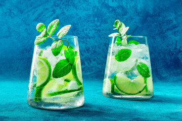 Lime lemonade, or limeade, in glasses with lime, mint, and plenty of ice. Fresh summer Mojito mocktail or cocktail, on a blue background