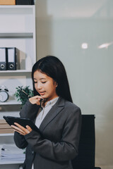 Young, smiling Asian businesswoman holding a jacket on her shoulder while using a mobile phone,...