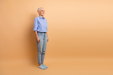 Confident mature woman posing in casual attire with a beige background, embracing elegance and...