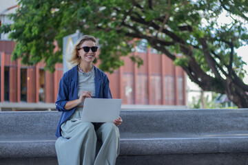 Obraz premium Smiling mature woman in suit with coffee and laptop on balcony. Confident and elegant entrepreneur contemplating success, happiness and desires.