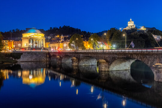 View of the illuminated Vittorio Emanuele I Bridge gracefully arching over the serene Po River with lights reflecting beautifully, Turin, Piedmont, Italy.