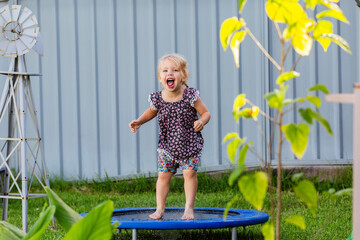 Toddler kid playing outside jumping on mini trampoline in backyard of home