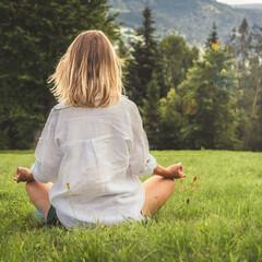 Young woman meditating in the meadow in the mountains. View from back.