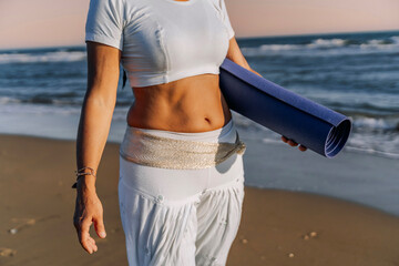 Close-up of woman in yoga outfit holding mat on the beach