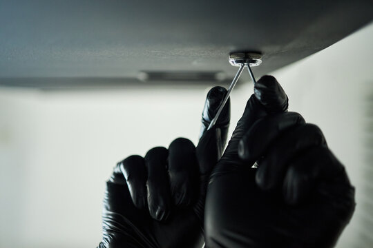 Hands of male burglar wearing black gloves picking lock on safe in office, to steal confidential business data or contract information, during break in or raid