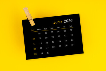 June 2026 black calendar with wooden clip on yellow color background.