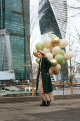pretty girl with big bunch of balloons in hand against city background on spring day
