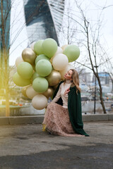pretty girl with big bunch of balloons in hand against city background on spring day
