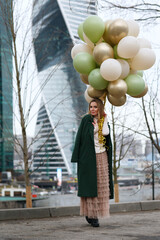 pretty girl with big bunch of balloons in hand against city background on spring day

