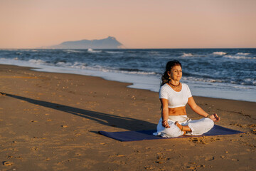 Woman meditating on beach during sunset yoga session