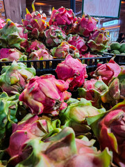 Vibrant close-up of fresh dragon fruits (pitaya) displayed in bulk at a local market or grocery store. The image showcases the exotic pink and green outer skin of the tropical fruit with rich color an