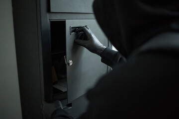 Unidentified male intruder wearing black gloves opening safe in dimly lit company office, focusing...