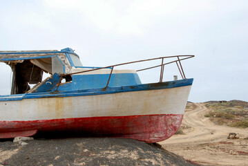 Abandoned blue and white fishing boat resting on volcanic terrain on the island of Graciosa, Canary Islands. The weathered boat contrasts with rugged natural surroundings in a coastal scene.