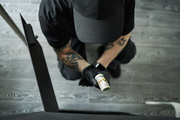 Tattooed anonymous young male burglar, wearing black gloves, kneeling on floor and stealing roll of...