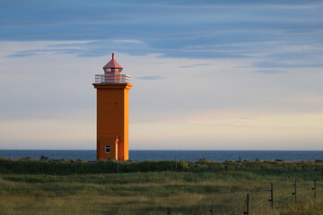 Stafnesviti lighthouse in the Reykjanes peninsula of Iceland, its bright orange contrasting with the blue sky and the green coastline during golden hour on July 3rd 2024
