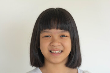 Cheerful young Asian girl smiles warmly at the camera against a white background. She wears a white shirt, radiating innocence, joy, and positivity in this close-up portrait