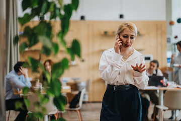 A woman communicates on her cellphone in a modern co working environment, standing out with her focus and determination amid a busy atmosphere of collaboration and productivity.