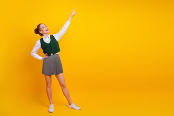 Cheerful Teen Student Excitedly Pointing Upward on Yellow Background, Representing Confidence,...