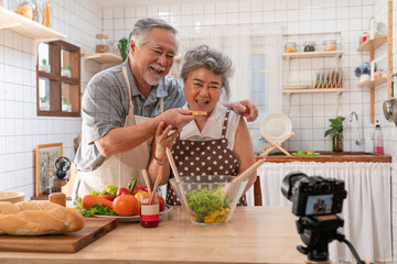 Happy elderly Asian couple take photo while cooking breakfast together in kitchen at home. Senior...