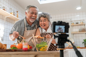 Happy elderly Asian couple take photo while cooking breakfast together in kitchen at home. Senior...