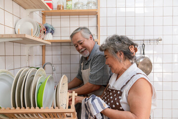 Happy elderly Asian couple washing dishes in the sink together in the kitchen at home. Senior retirement in love with healthy