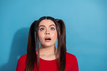 Surprised young woman in stylish red top against blue background showing expression of amazement...