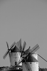 Black and white image of three traditional windmills aligned on a ridge under a clear sky. The...