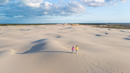A couple strolls hand in hand across the expansive white sand dunes of Rabjerg Mile, Denmark. during golden hour. The soft light and gentle breeze create a tranquil atmosphere
