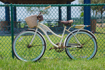 Fototapeta premium Vintage Bicycle with Basket Leaning Against Fence in Sunny Outdoor Setting with Bay in back Gulfport, FL Charming rests against a chain link fence on a sunny day. The scene captures a peaceful moment 