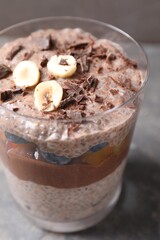 Delicious chocolate pudding with chia seeds, nuts and berries in glass on grey table, closeup