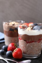 Delicious chocolate puddings with chia seeds, nuts and berries in glasses on table, closeup