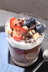 Delicious chocolate pudding with chia seeds, nuts and berries in glass on grey table, closeup
