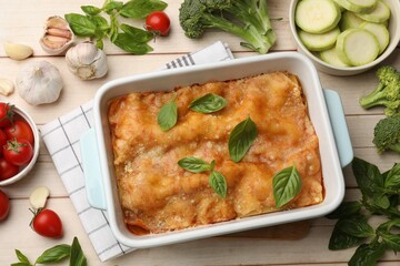 Tasty vegetarian lasagna in baking dish and ingredients on white wooden table, flat lay