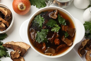 Tasty soup with mushrooms and parsley in bowl on white table, flat lay