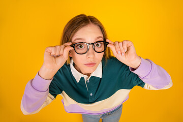 Focused young woman in trendy casual clothing adjusting glasses against a bright yellow background