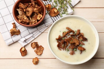 Tasty cream soup, thyme and dry chanterelle mushrooms on light wooden table, flat lay