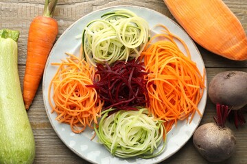 Different noodles and vegetables on wooden table, flat lay