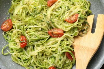 Tasty zucchini noodles with tomatoes, thyme and turner on frying pan, closeup