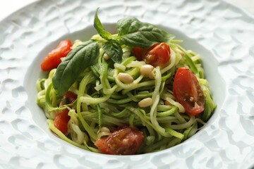 Tasty zucchini noodles with tomatoes, pine nuts and basil, closeup