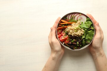 Healthy vegetarian food. Woman with delicious Buddha bowl at light wooden table, top view. Space...