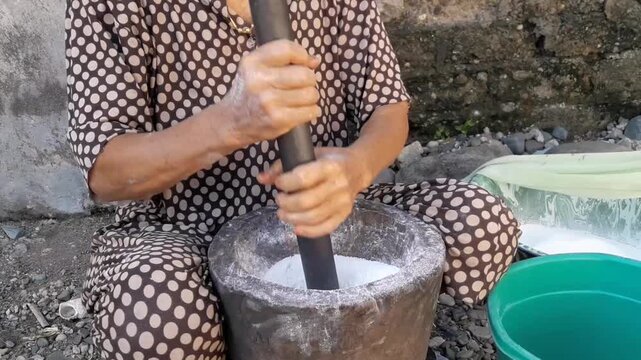 A woman manually pounds rice using a mortar or pestle, a traditional tool for grinding rice into flour. This traditional method is still used in Aceh Province.