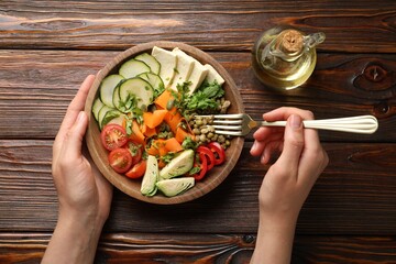 Healthy vegetarian food. Woman eating delicious Buddha bowl at wooden table, top view